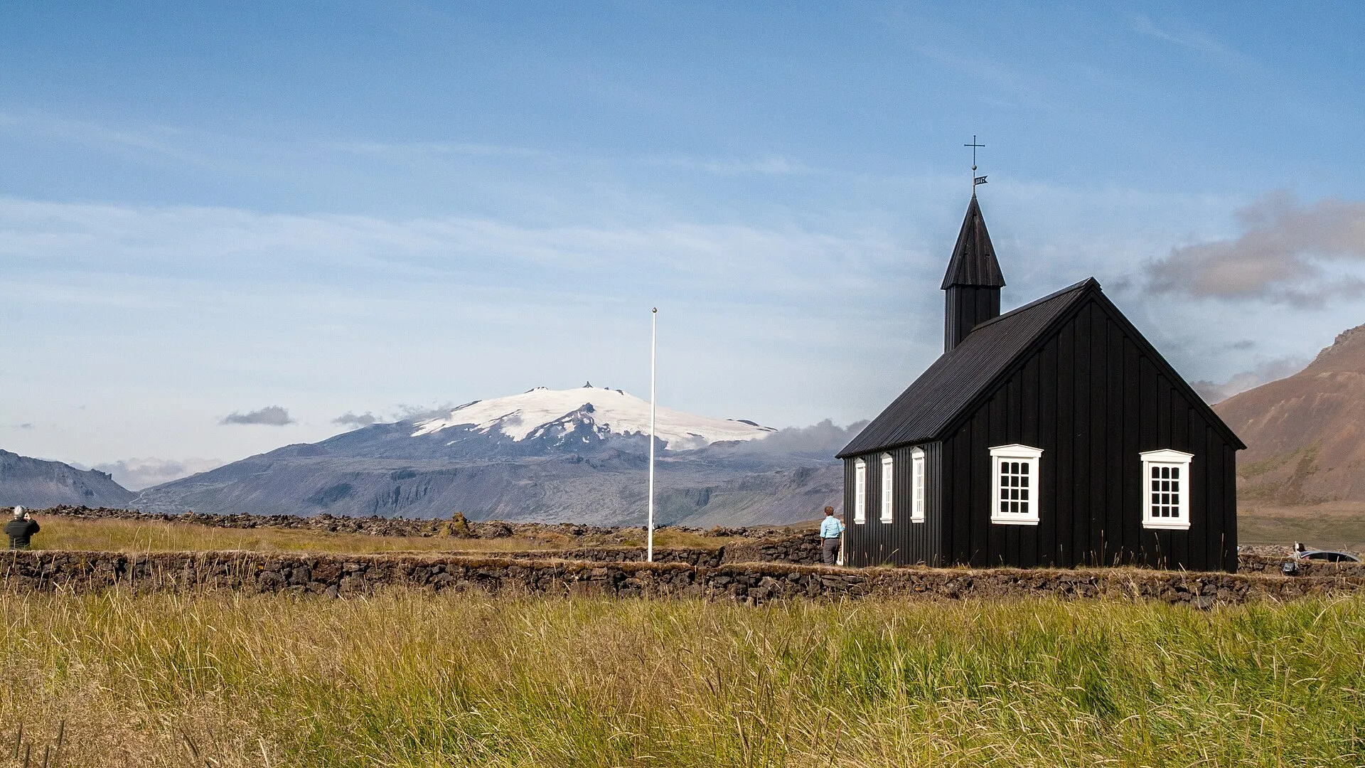 Czarny drewniany kościół w Búðir z białymi oknami, w tle ośnieżony stożek Snæfellsjökull
