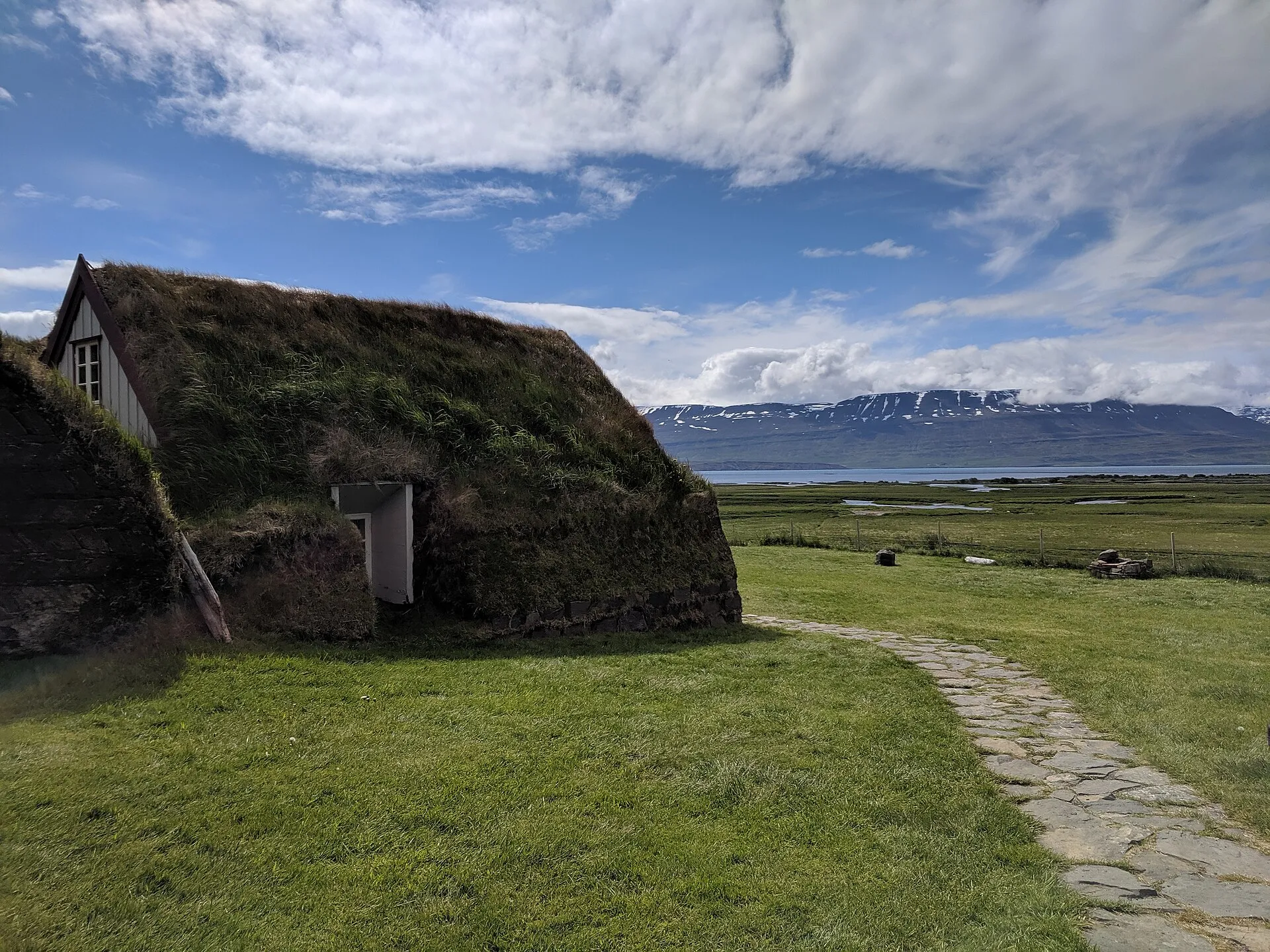 Tradycyjny islandzki dom darniowy z porośniętym trawą dachem, w tle fiord i góry
