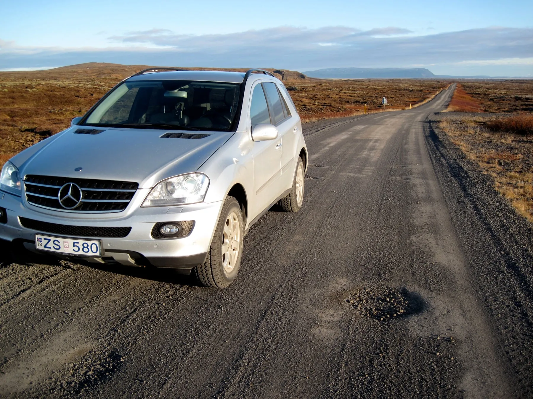 Srebrny SUV na szutrowej drodze wśród rudych wrzosowisk, w tle płaska góra