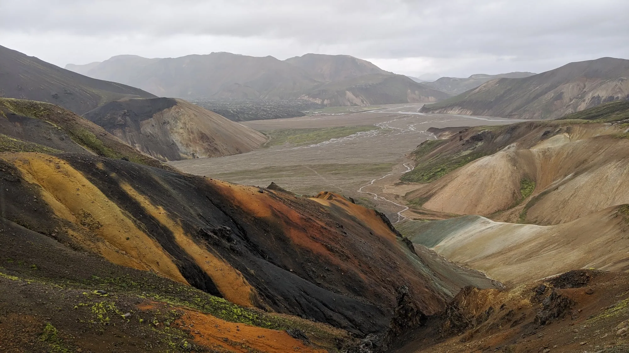 Pasmowe, rdzawe i czarne zbocza ryolitowe nad szeroką doliną rzeczną w Landmannalaugar