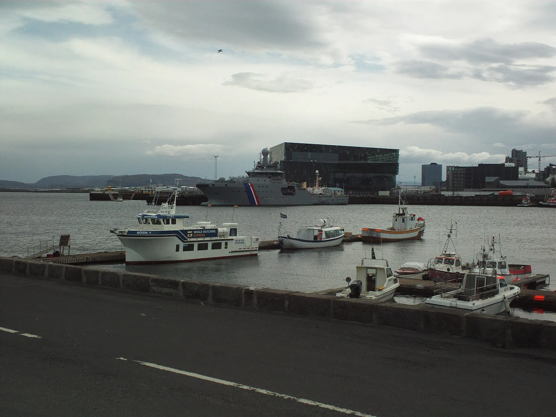 Stary port w Reykjavíku – łodzie przy nabrzeżu, statek straży przybrzeżnej i szklany budynek Harpy w tle