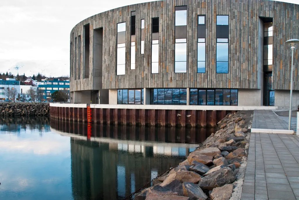 Okrągły budynek centrum kultury Hof w Akureyri odbijający się w wodzie przy nabrzeżu