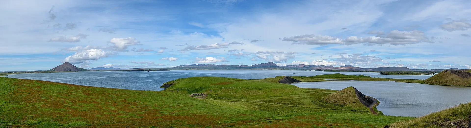 Panorama jeziora Mývatn z zielonymi pagórkami i wysepkami, w tle płaskie góry