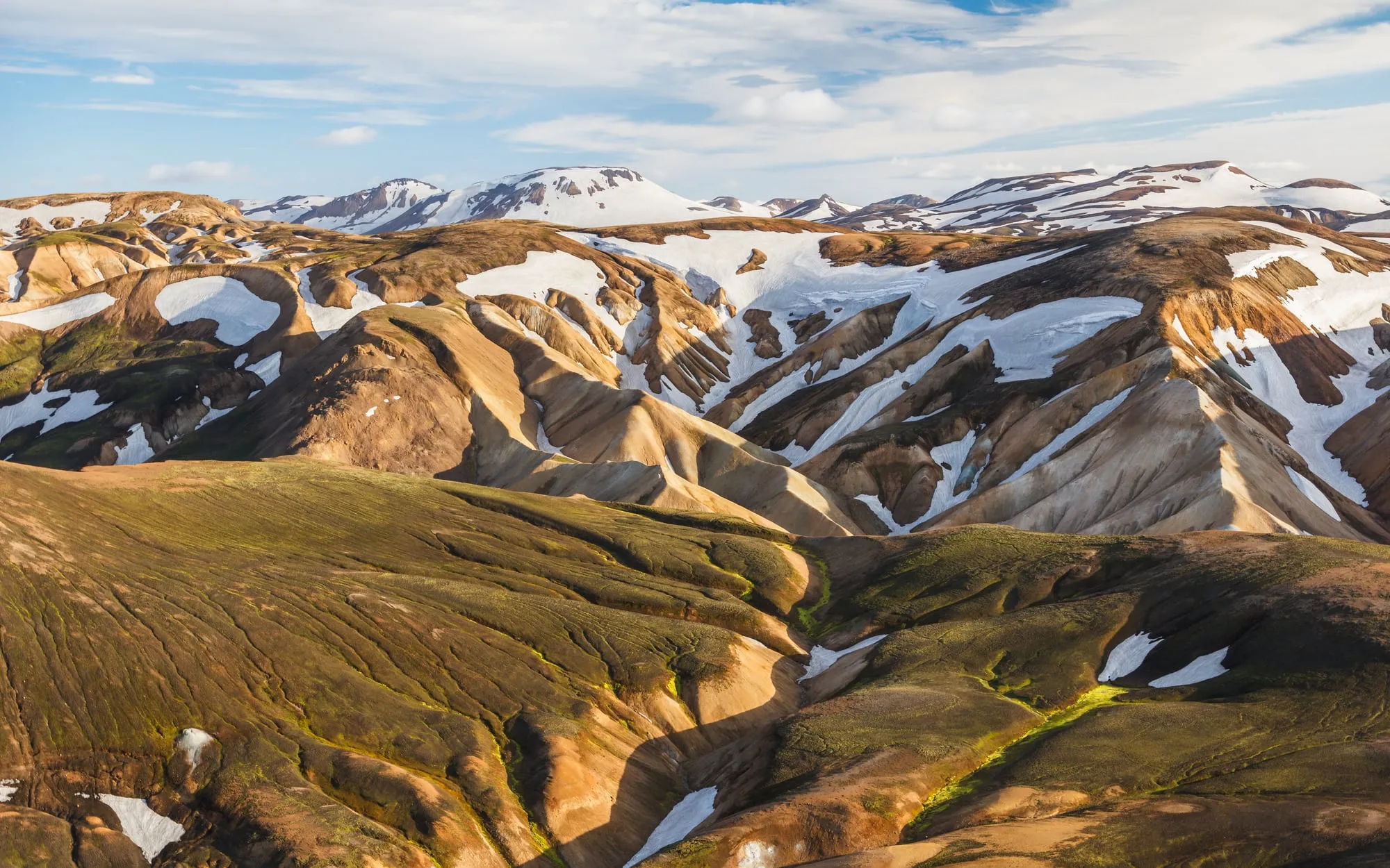 Ośnieżone i rdzawe ryolitowe wzgórza w Landmannalaugar w popołudniowym słońcu