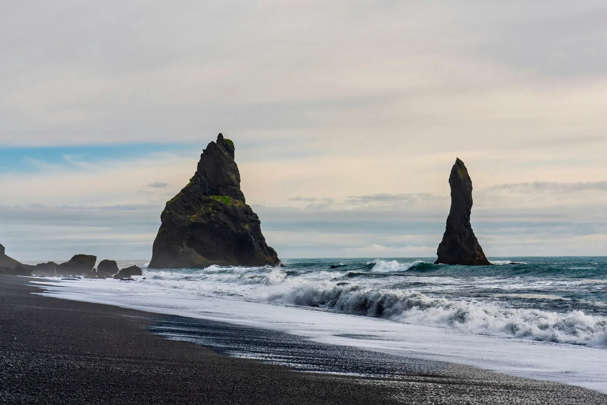 Skały Reynisdrangar wystające z oceanu, fale rozbijające się o czarną plażę Reynisfjara