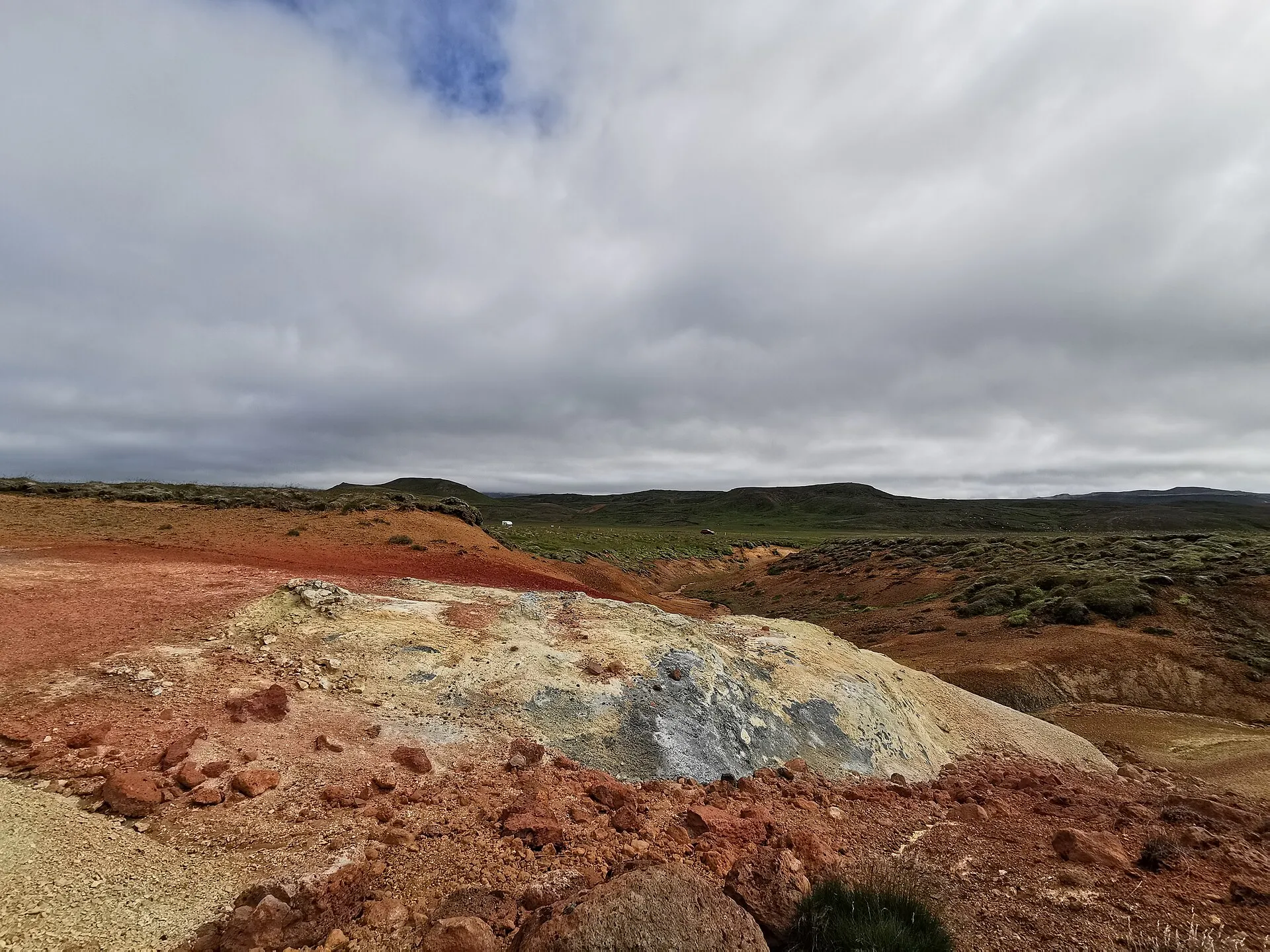 Kolorowa, czerwono-żółta ziemia na polu geotermalnym Krýsuvík, w tle zielone wzgórza