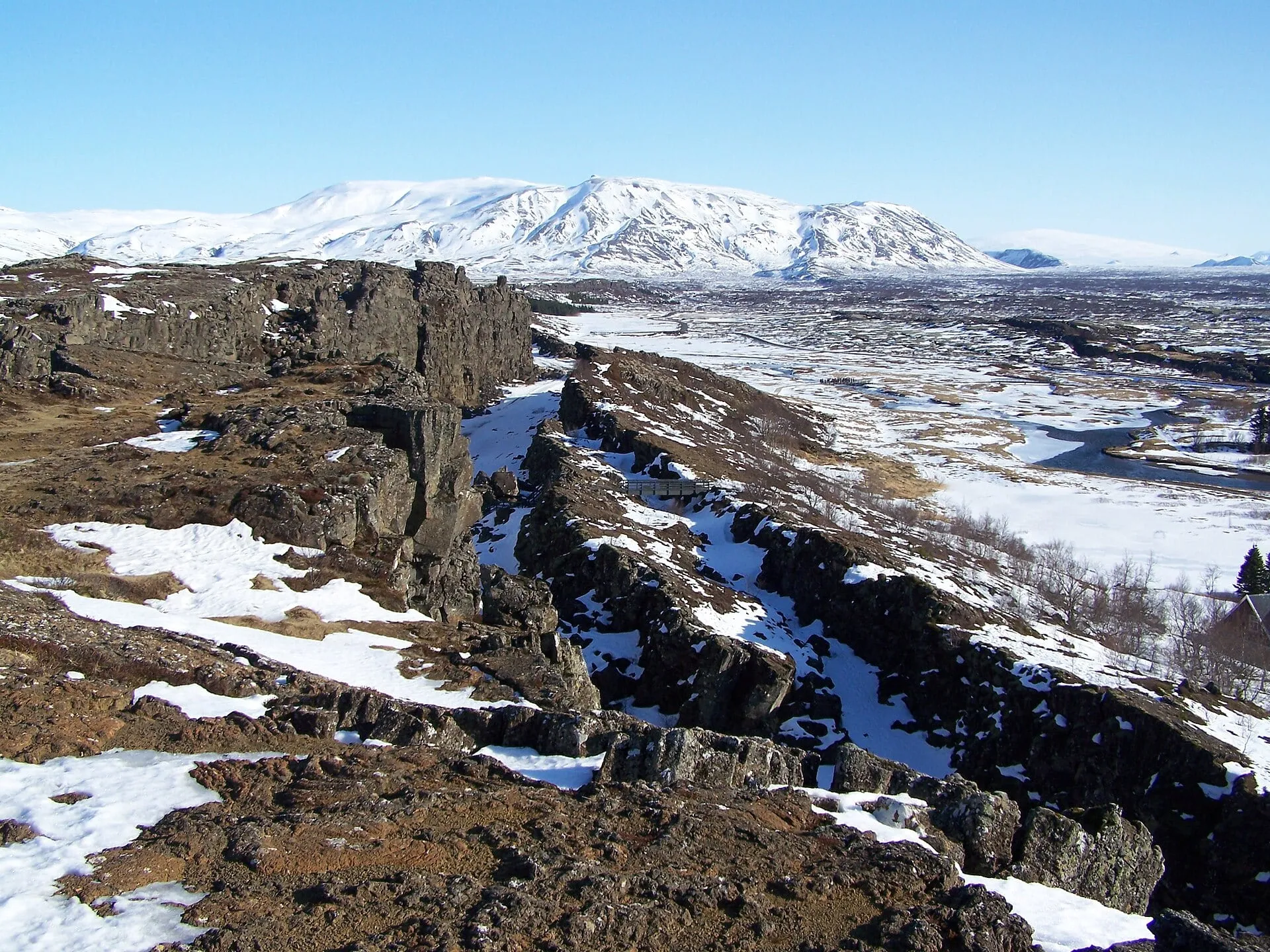 Krajobraz Parku Narodowego Þingvellir zimą – równoległe szczeliny i uskoki w skałach, w tle ośnieżona góra