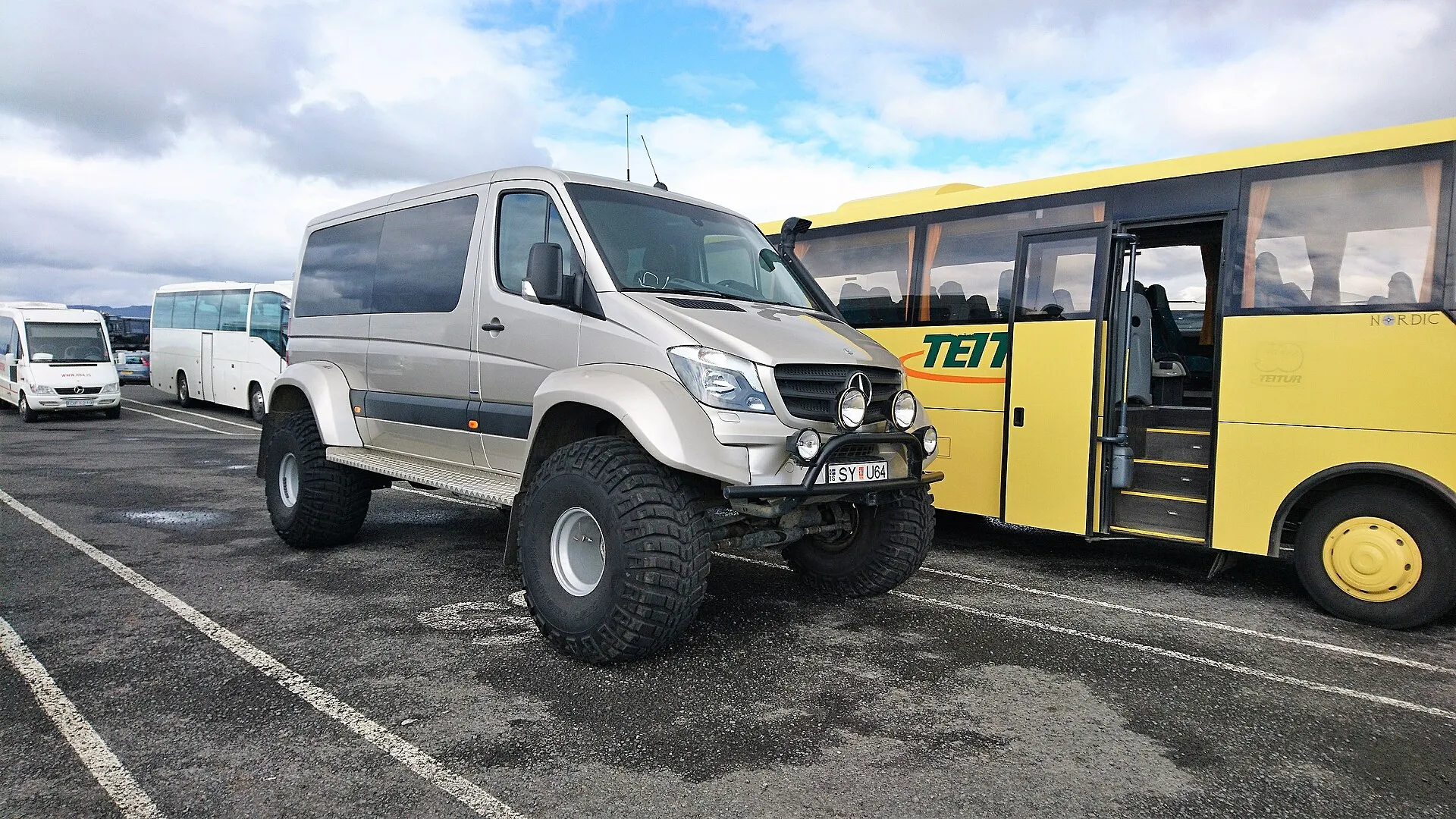 Superjeep na ogromnych terenowych oponach zaparkowany obok autokaru na parkingu