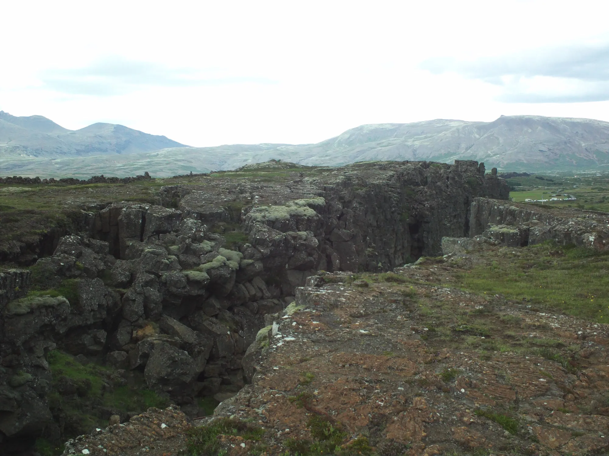 Szczeliny i ściany lawowe w Parku Narodowym Þingvellir, w tle góry