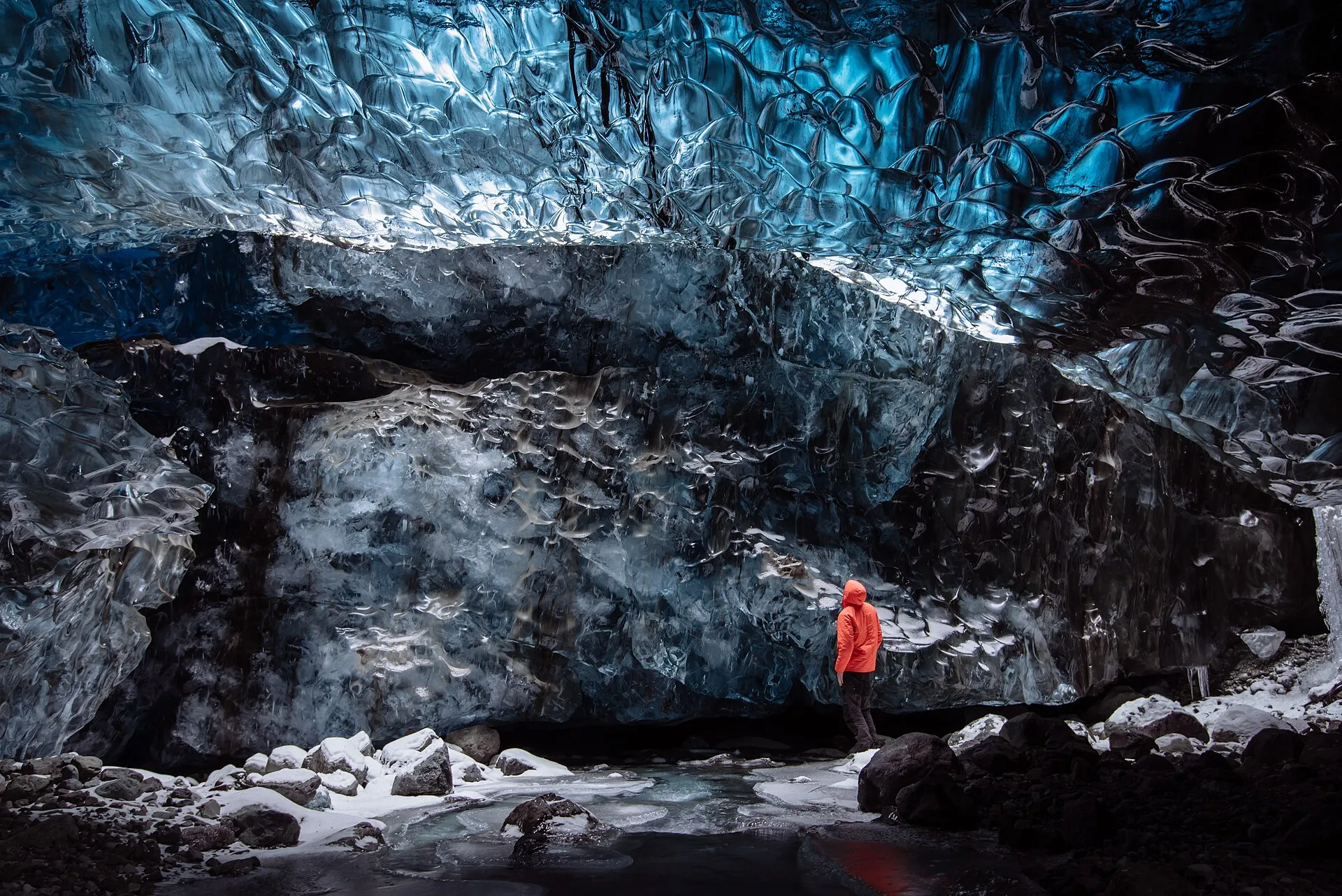 Turysta w czerwonej kurtce w niebieskiej jaskini lodowej pod Vatnajökull