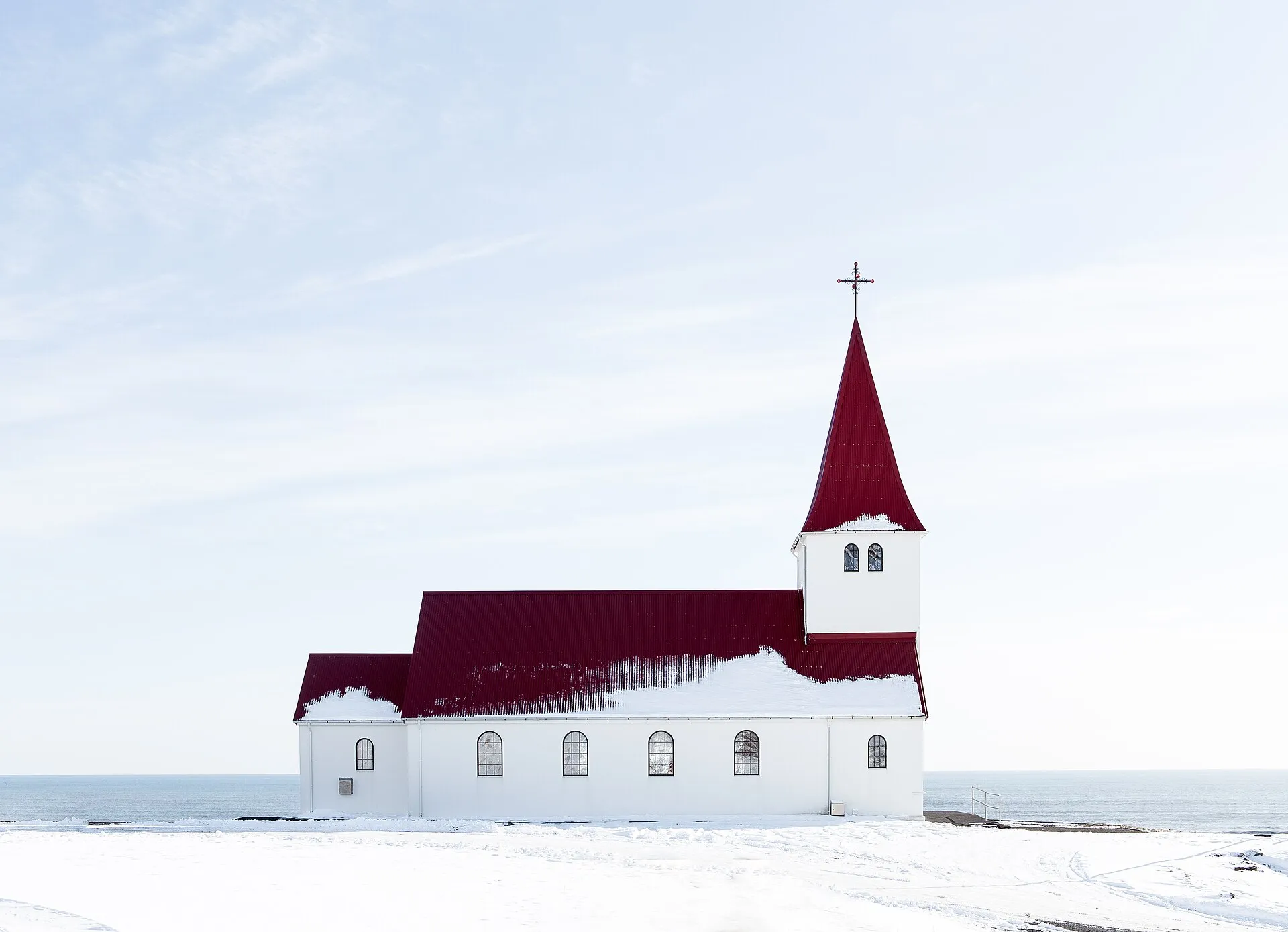 Biały kościół z czerwonym dachem w Vík zimą, w tle ocean